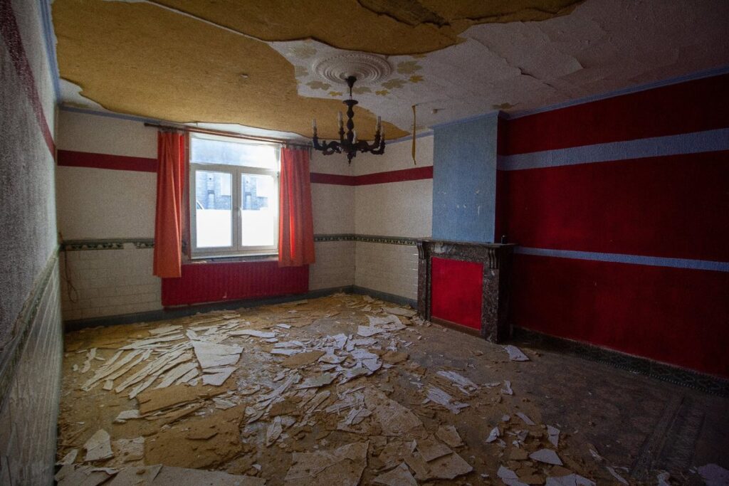Pièce aux murs rouges dont le plafond est tombé au sol, dans une maison en mauvais état visitée en Belgique